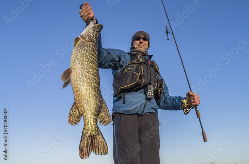 Happy fisherman holding big pike fish trophy and fishing rod