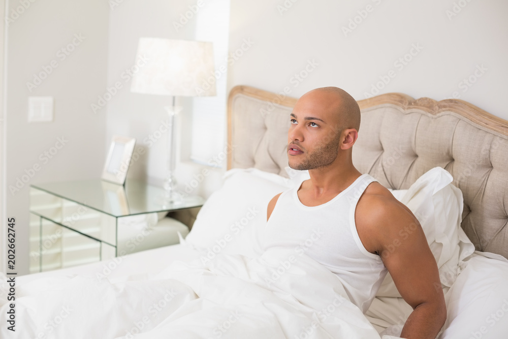 Thoughtful young bald man sitting in bed Thoughtful young bald man sitting in bed