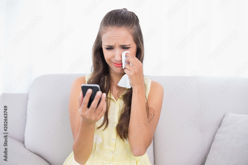 Crying attractive brunette holding mobile phone and tissue Crying attractive brunette holding mobile phone and tissue