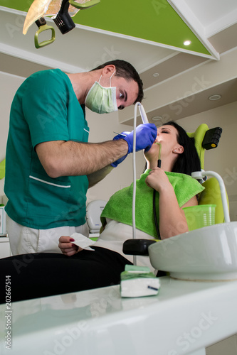 Young woman sitting on dental chair while young male dentist fixes her teeth. 