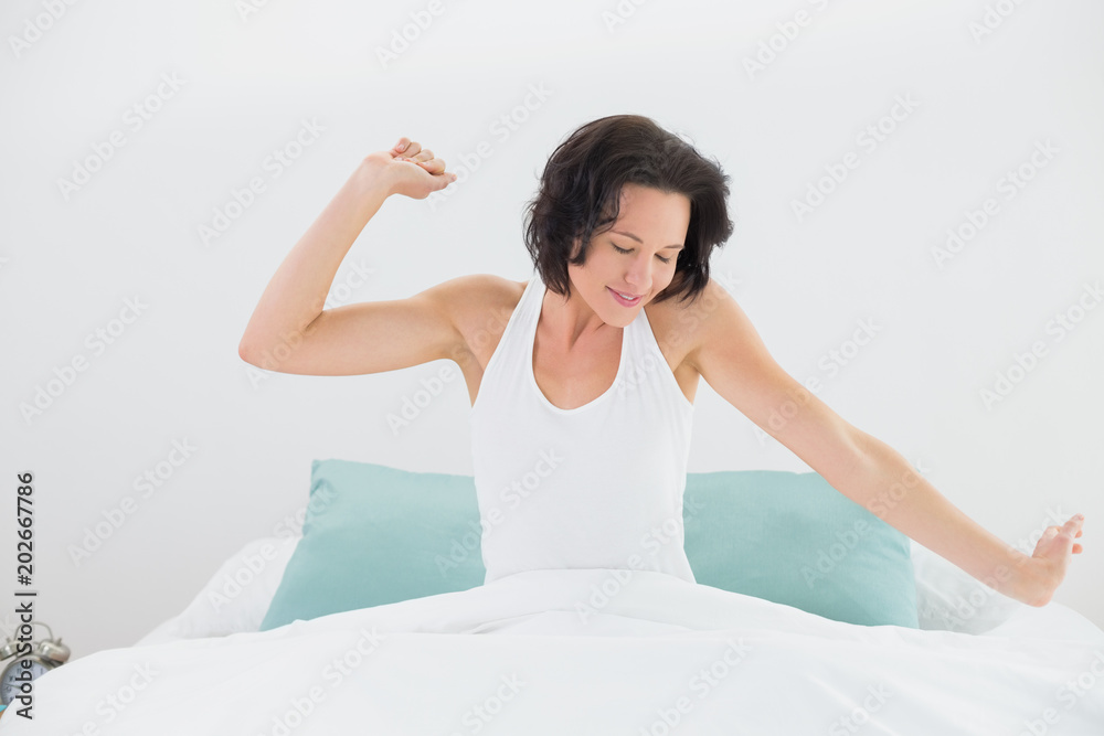 Young woman stretching arms in bed