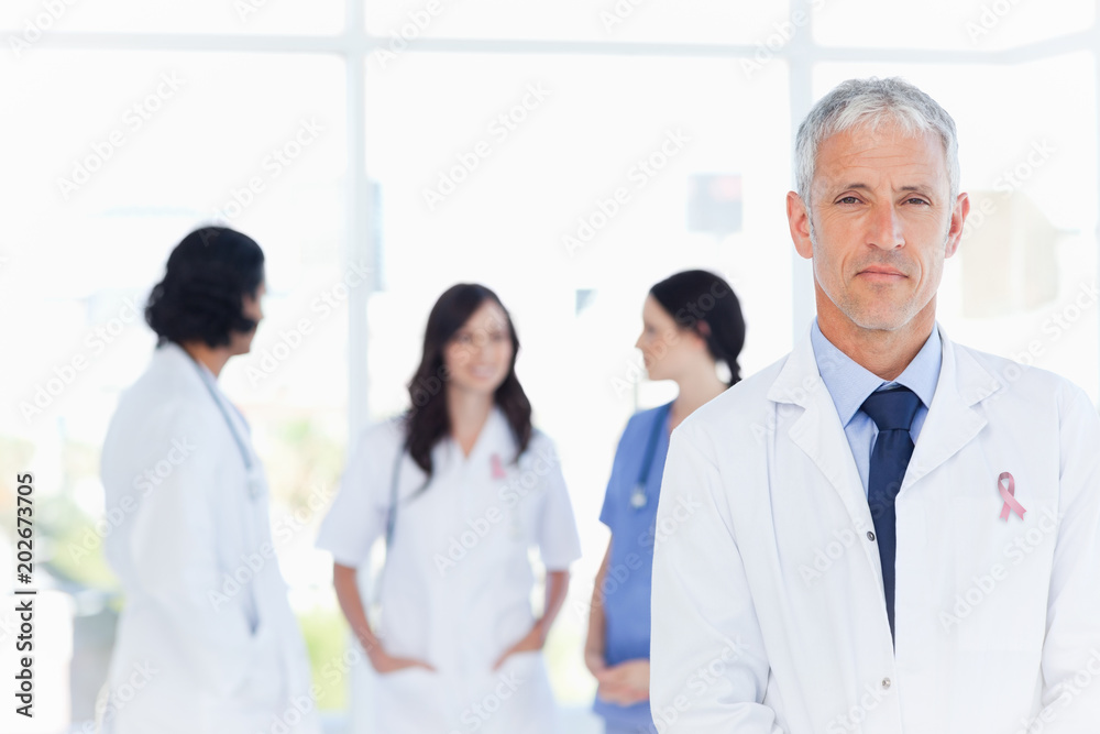 Mature doctor standing in the foreground wearing  breast cancer awareness ribbon