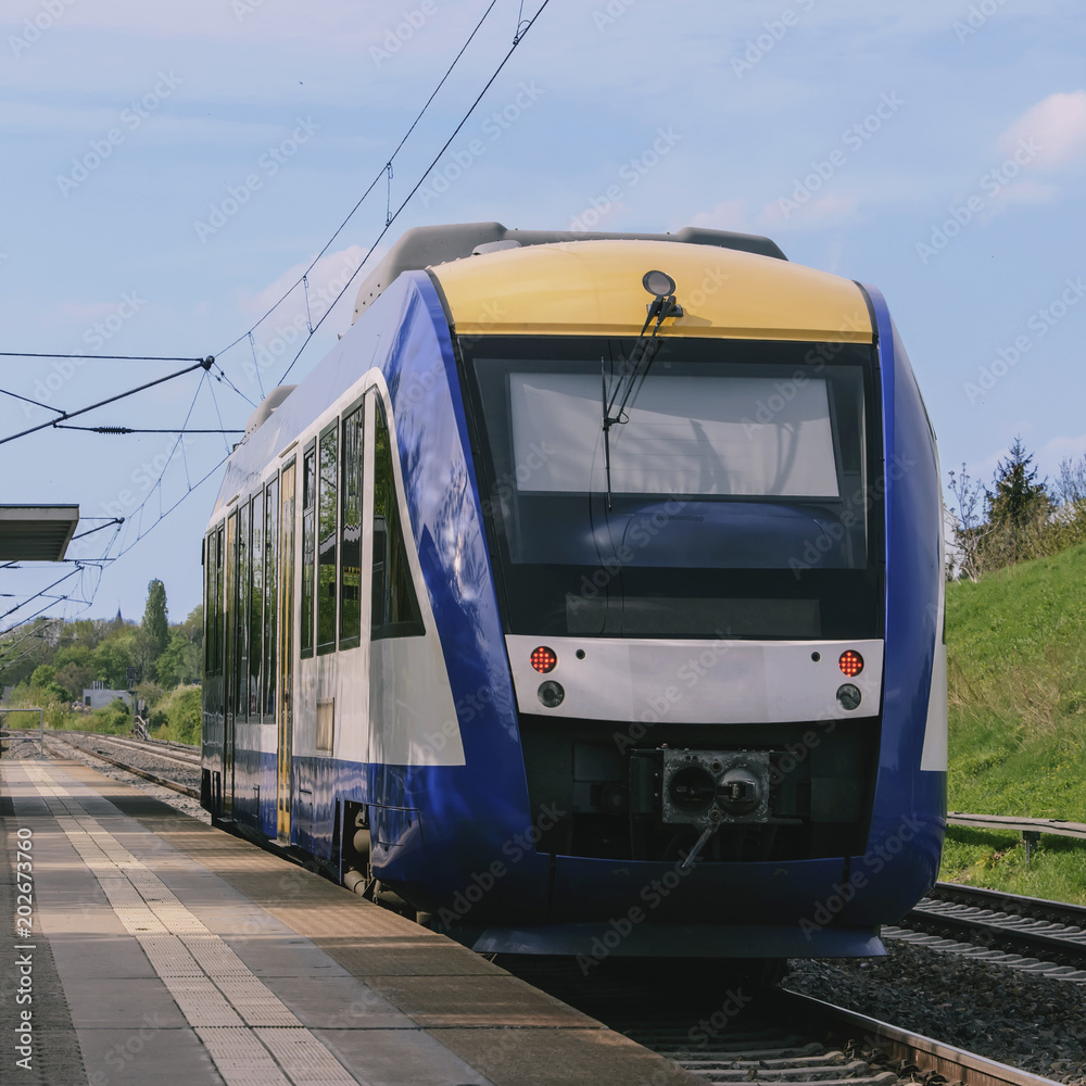 short passenger train stands on a deserted platform in a picturesque countryside.