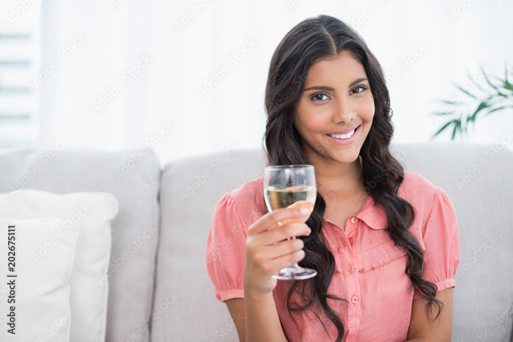 Happy cute brunette sitting on couch holding white wine glass Happy cute brunette sitting on couch holding white wine glass