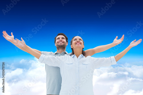 Cute couple standing with arms out against blue sky over clouds