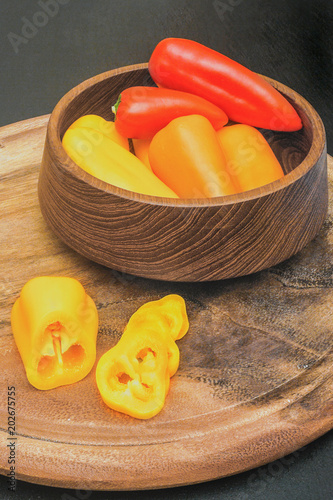 Red, orange and yellow mini paprika in wooden utensils and on a cutting board photo