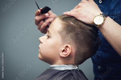 Barber is making haircut to boy in barbershop.