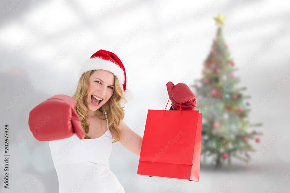 Festive blonde with boxing gloves and shopping bag against blurry christmas tree in room