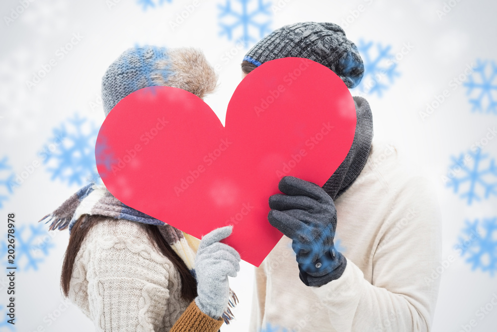 Attractive young couple in warm clothes holding red heart against snowflakes