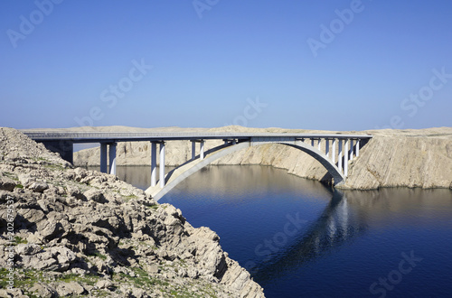Bridge above the blue sea surface with reflection in the water, between the rocky land