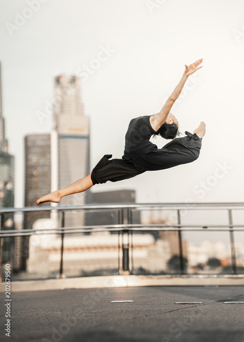 Passion... Young woman athlete performs a perfect leap high up, on a bridge  with background of skyscrapers
