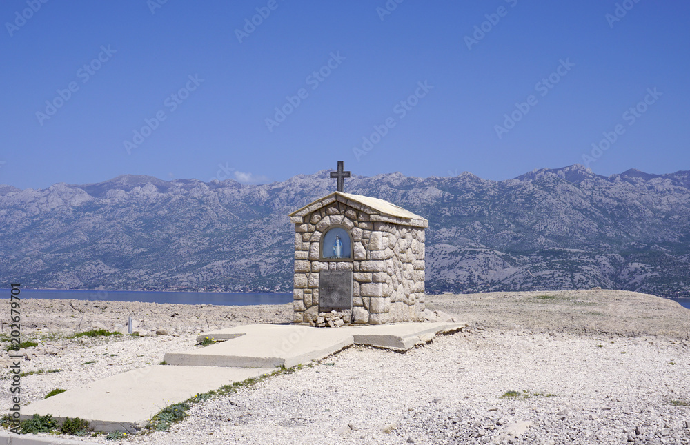 Fototapeta premium Small stone chapel with Mary statue in front of mountain Velebit in Croatia