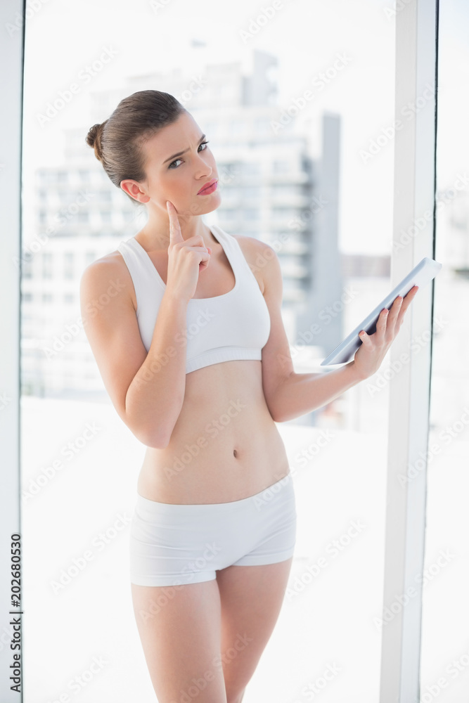 Thoughtful fit brown haired model in sportswear using a tablet pc