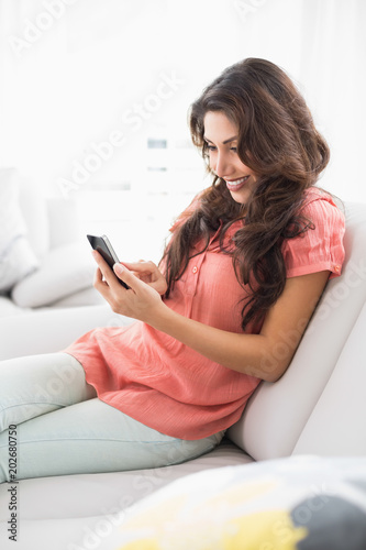 Happy brunette sitting on her couch using her smartphone