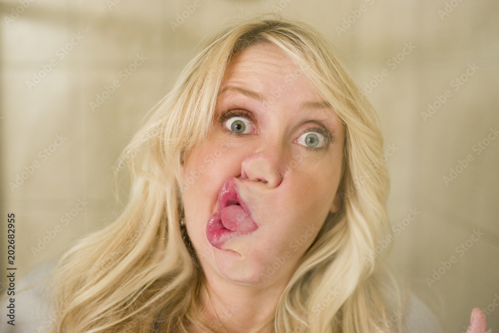 Wall Mural Blonde woman smashing face against window silly look