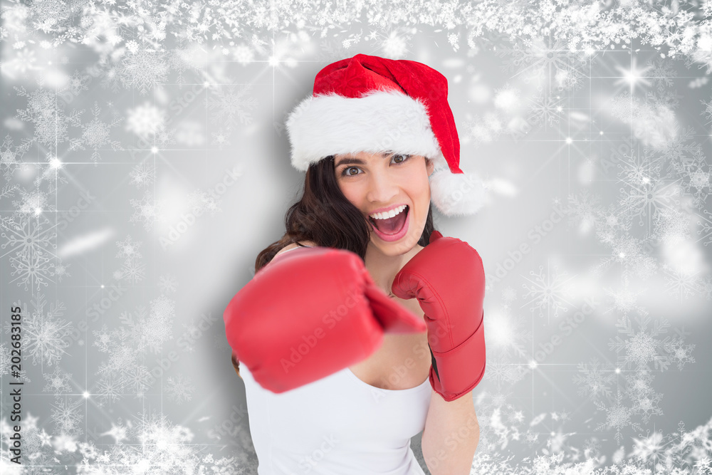 Festive brunette in boxing gloves punching against white snowflake design on grey Festive brunette in boxing gloves punching against white snowflake design on grey