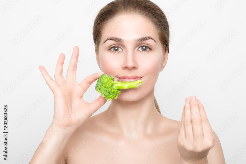 Beautiful woman holds broccoli in her right hand and says delicious with her left. Beautiful woman holds broccoli in her right hand and says delicious with her left.
