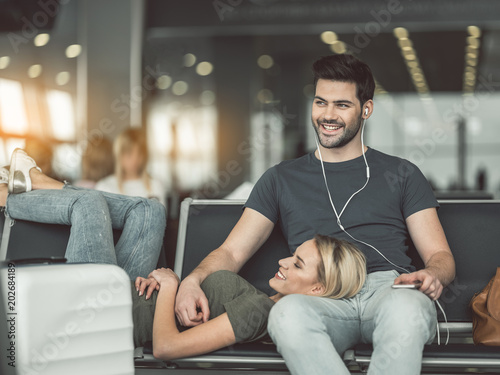 Outgoing female lying on smiling boy. He hearing song with appliance. Happy couple locating in airport concept