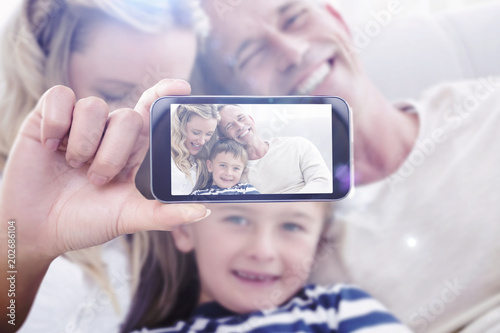 Hand holding smartphone showing against happy parent tickling her cute son on the couch