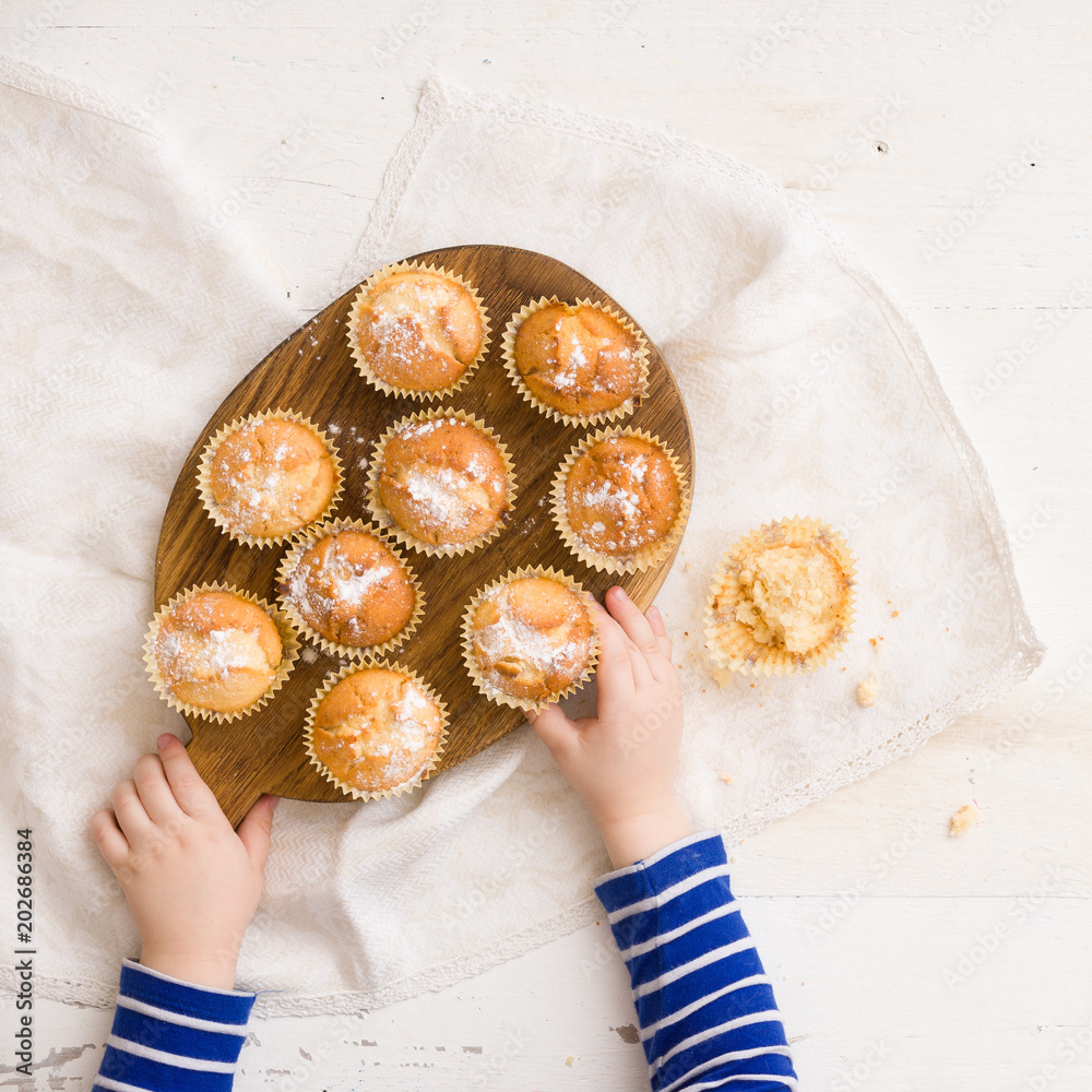 Φωτογραφία Top view on child's hands holding wooden board with freshly baked home muffins on white table background
