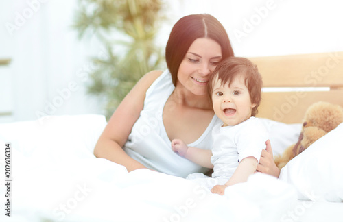 Beautiful young mother  with a baby  lying in bed and smiling