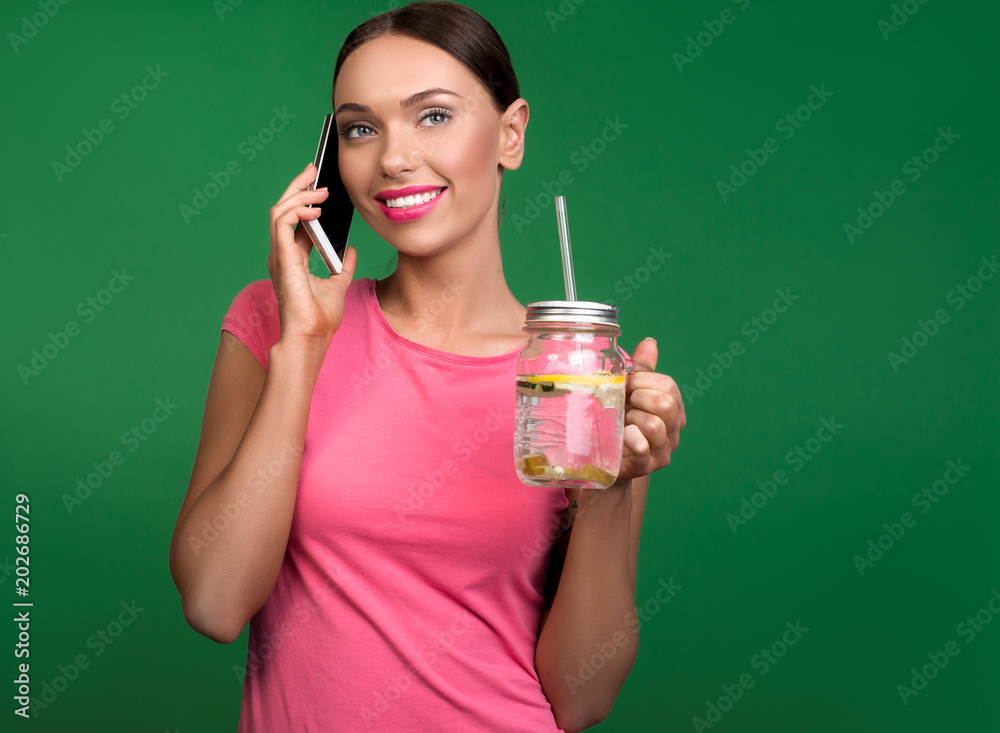 Waist up portrait of smiling girl talking by smartphone with lemonade in hand. Copy space in right side. Isolated on background Waist up portrait of smiling girl talking by smartphone with lemonade in hand. Copy space in right side. Isolated on background