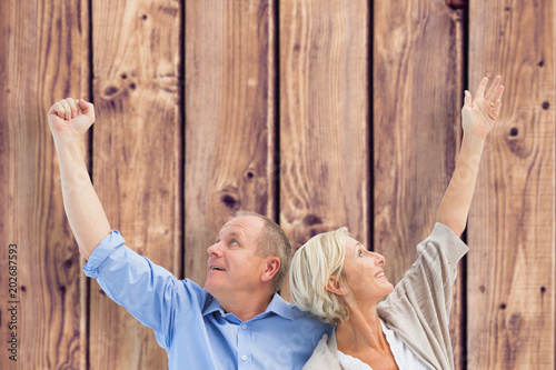 Happy mature couple with hands up against wooden planks background
