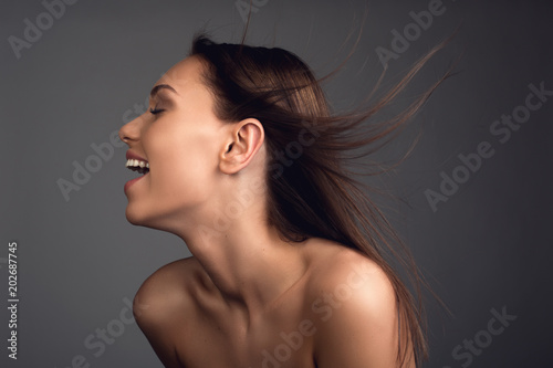 Profile of contented woman with hair blowing. Her shoulders are undressed and skin is pure. Isolated on background