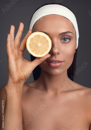 Portrait of nude woman with perfect skin covering one eye with orange slice. Isolated on background