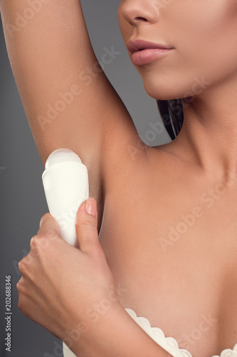 Close up of female person taking care of her hygiene. She using roll on antiperspirant under the arms