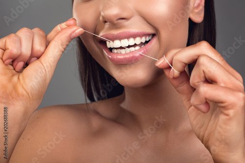 Close up of satisfied longhaired girl using dental floss. Isolated on background