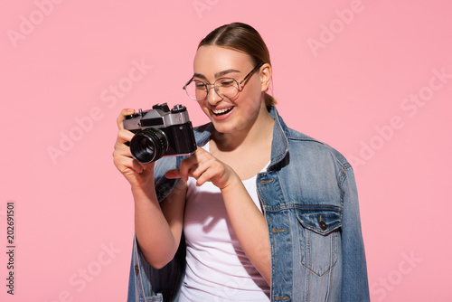 Portrait of happy girl watching photos on camera screen. She is standing and smiling. Isolated