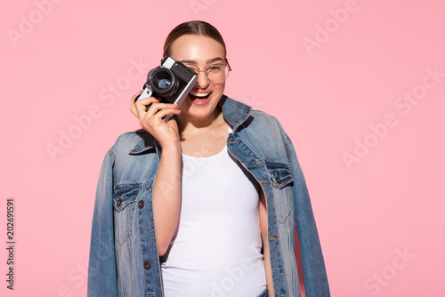 Smile. Waist up portrait of excited girl taking photo and smiling. Isolated on pink background