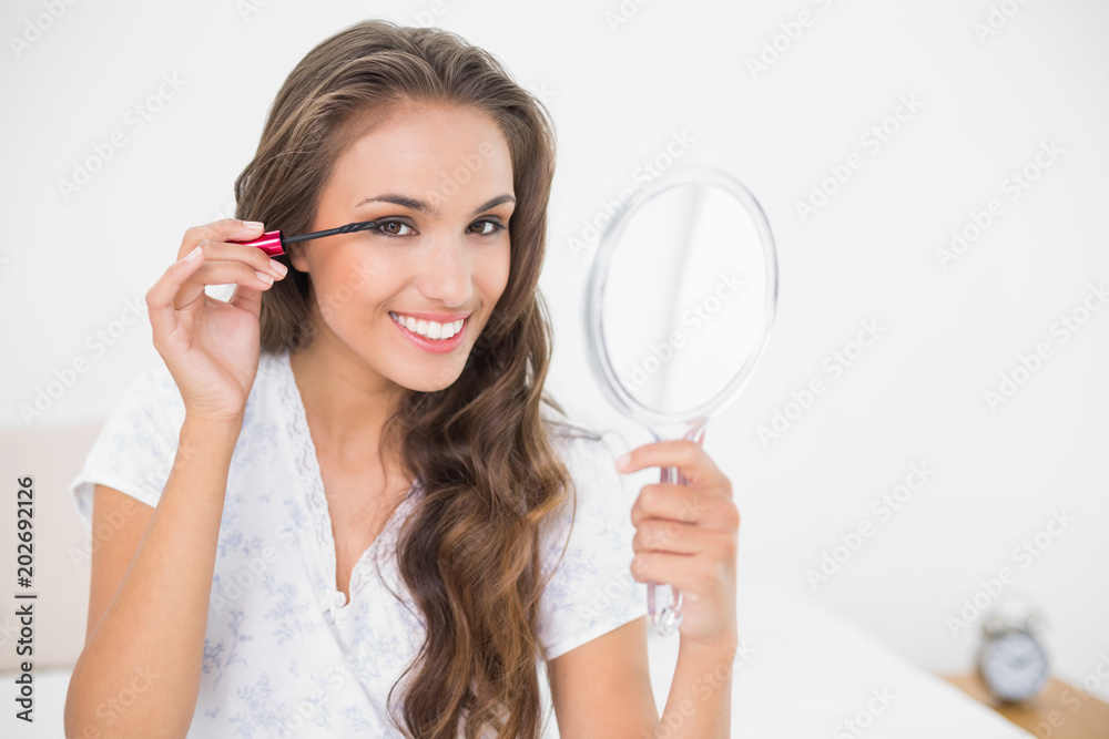 Smiling attractive brunette applying mascara and holding mirror Smiling attractive brunette applying mascara and holding mirror