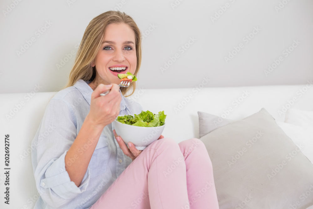 Smiling casual blonde sitting on couch eating salad Smiling casual blonde sitting on couch eating salad
