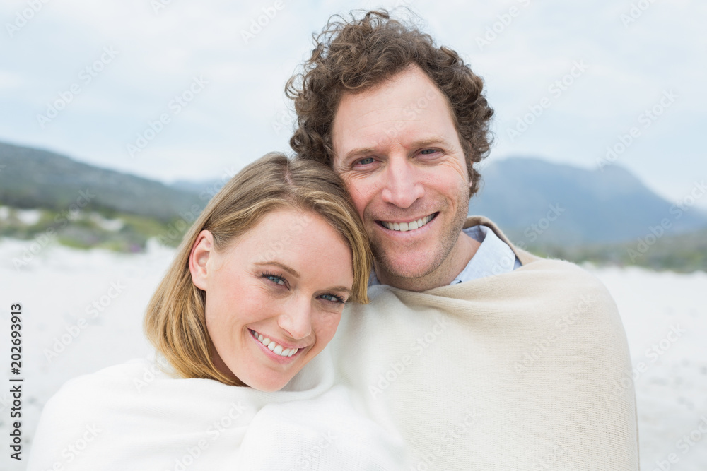 Smiling couple wrapped in blanket at beach Smiling couple wrapped in blanket at beach