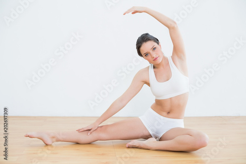 Toned woman stretching hand and leg in fitness studio