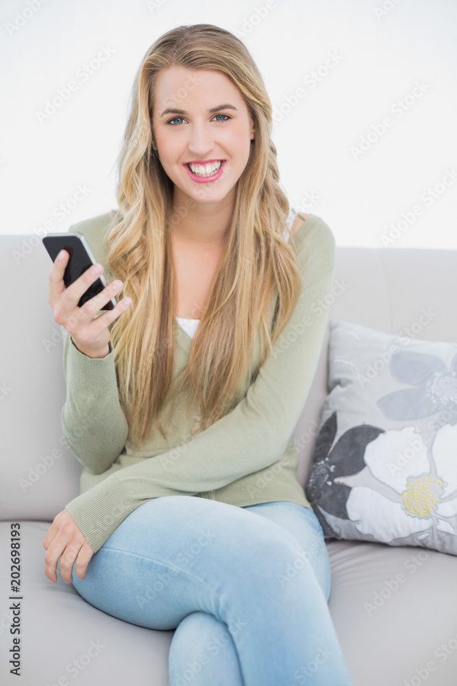 Cheerful pretty blonde text messaging while sitting on cosy sofa Cheerful pretty blonde text messaging while sitting on cosy sofa