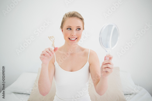 Natural happy blonde holding mirror and eyelash curler