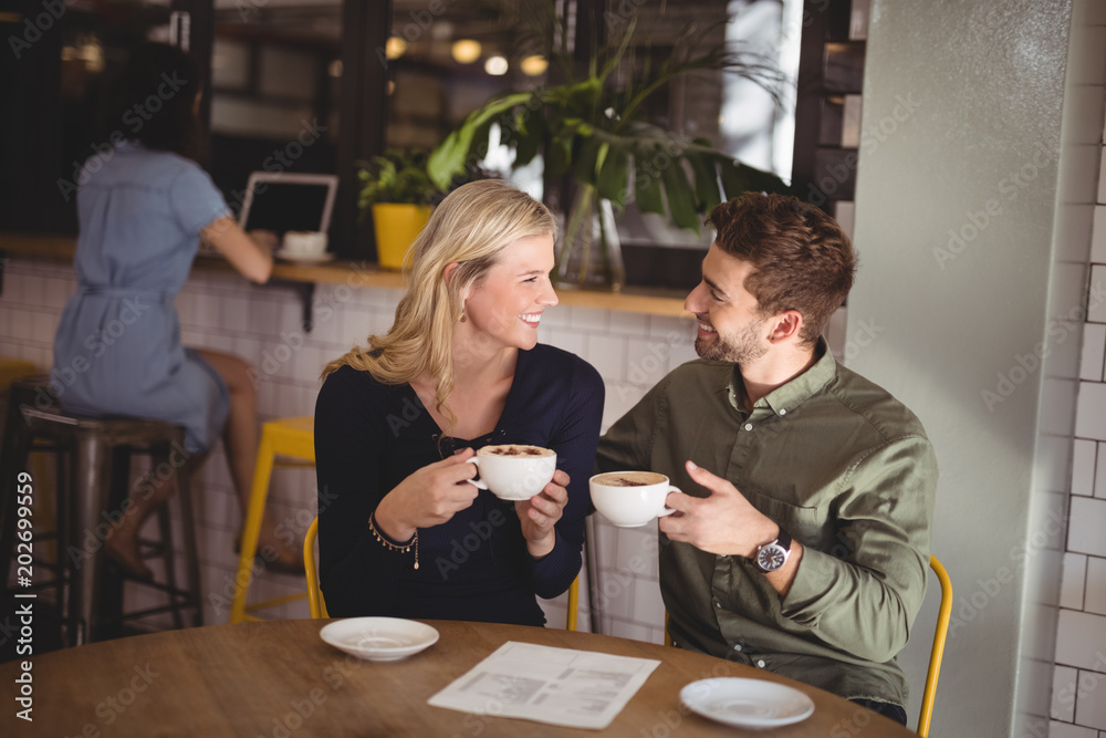 Smiling couple holding fresh coffee cups while sitting at cafeteria