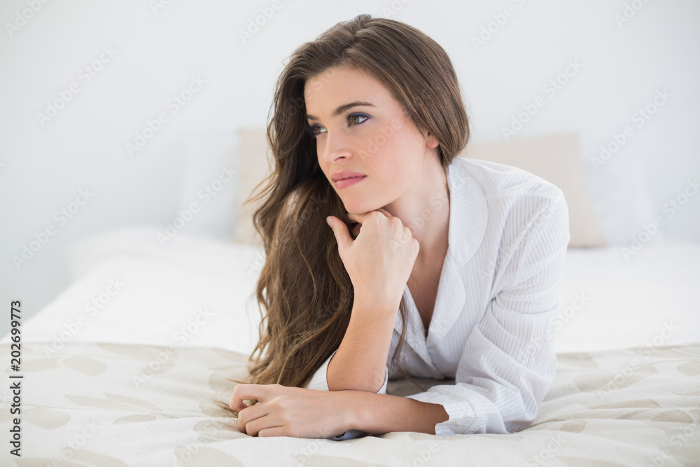 Thinking casual brown haired woman in white pajamas lying on her bed Thinking casual brown haired woman in white pajamas lying on her bed
