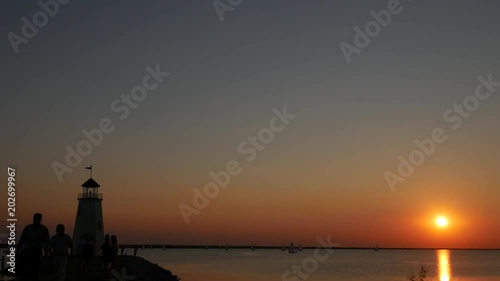 Wallpaper Mural Wide shot of sunset at the lake with a lighthouse and the silhouette of unrecognizable people walking Torontodigital.ca