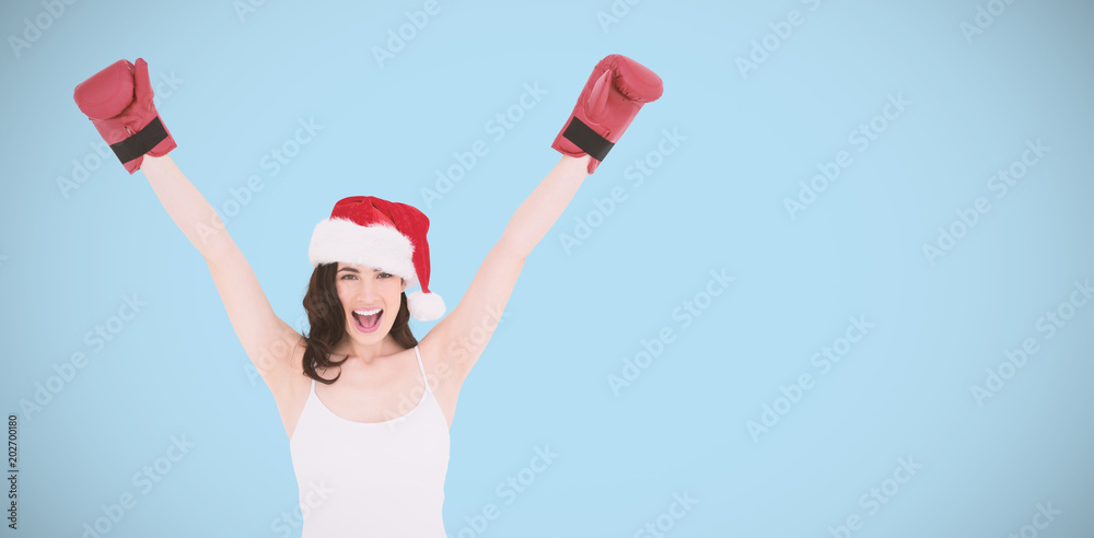 Festive brunette in boxing gloves cheering against blue background Festive brunette in boxing gloves cheering against blue background