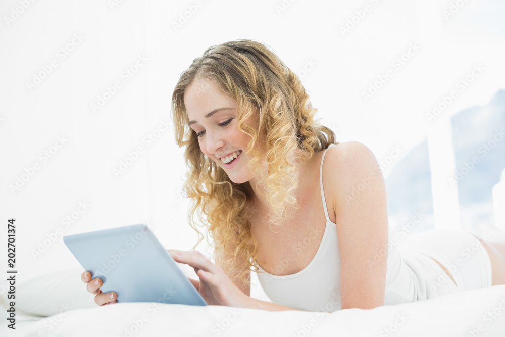 Pretty smiling blonde lying in bed using tablet Pretty smiling blonde lying in bed using tablet