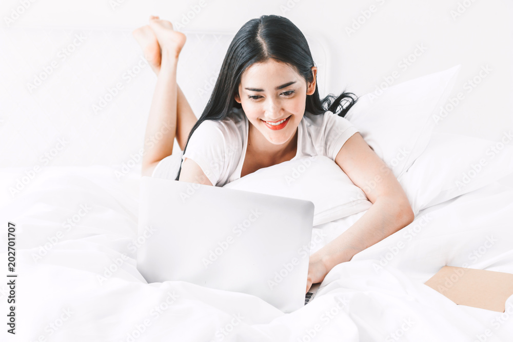 Happy woman relaxing and using digital laptop computer on the bed at home.woman checking social apps and working with smartphone Happy woman relaxing and using digital laptop computer on the bed at home.woman checking social apps and working with smartphone