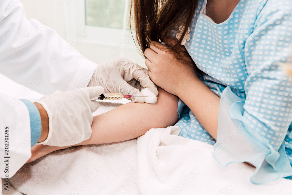 Doctor in protective gloves giving injection with little girl child on doctors table in hospital.healthcare and medicine Doctor in protective gloves giving injection with little girl child on doctors table in hospital.healthcare and medicine