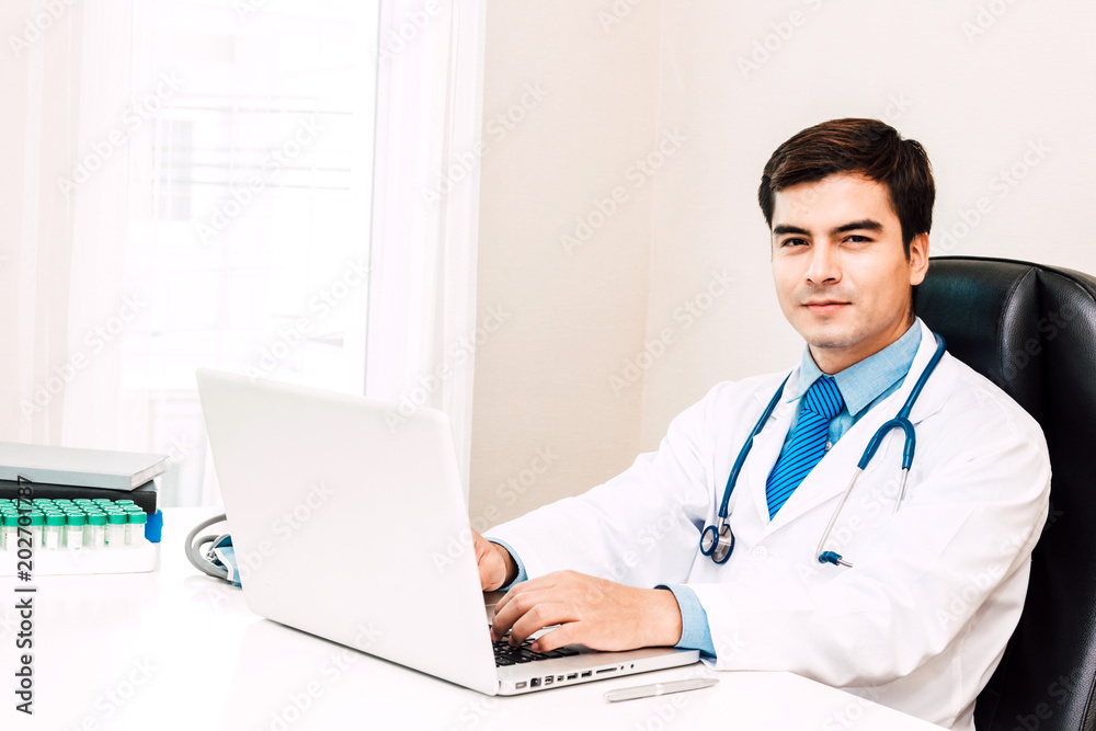 Doctor smiling and looking at camera with stethoscope working on laptop computer in hospital.healthcare and medicine Doctor smiling and looking at camera with stethoscope working on laptop computer in hospital.healthcare and medicine