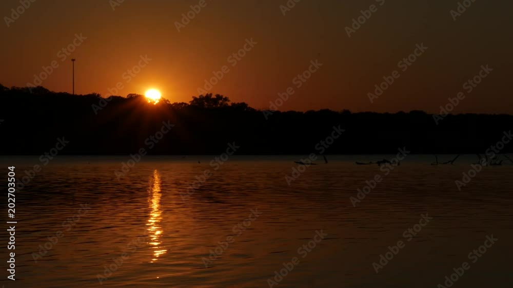 Steady shot of water flowing in the lake with a beautiful sun setting in the horizon Steady shot of water flowing in the lake with a beautiful sun setting in the horizon