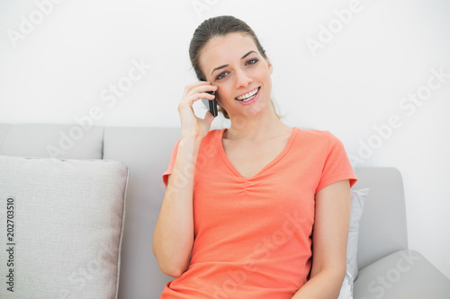 Pretty casual woman phoning with her smartphone sitting on couch