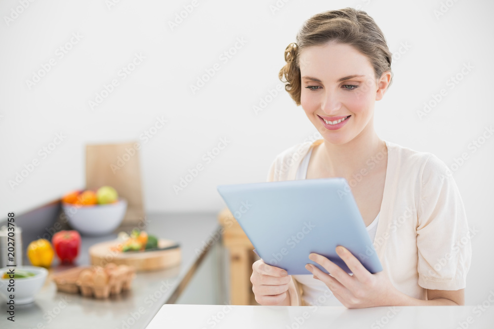 Content peaceful woman using her tablet sitting in her kitchen Content peaceful woman using her tablet sitting in her kitchen